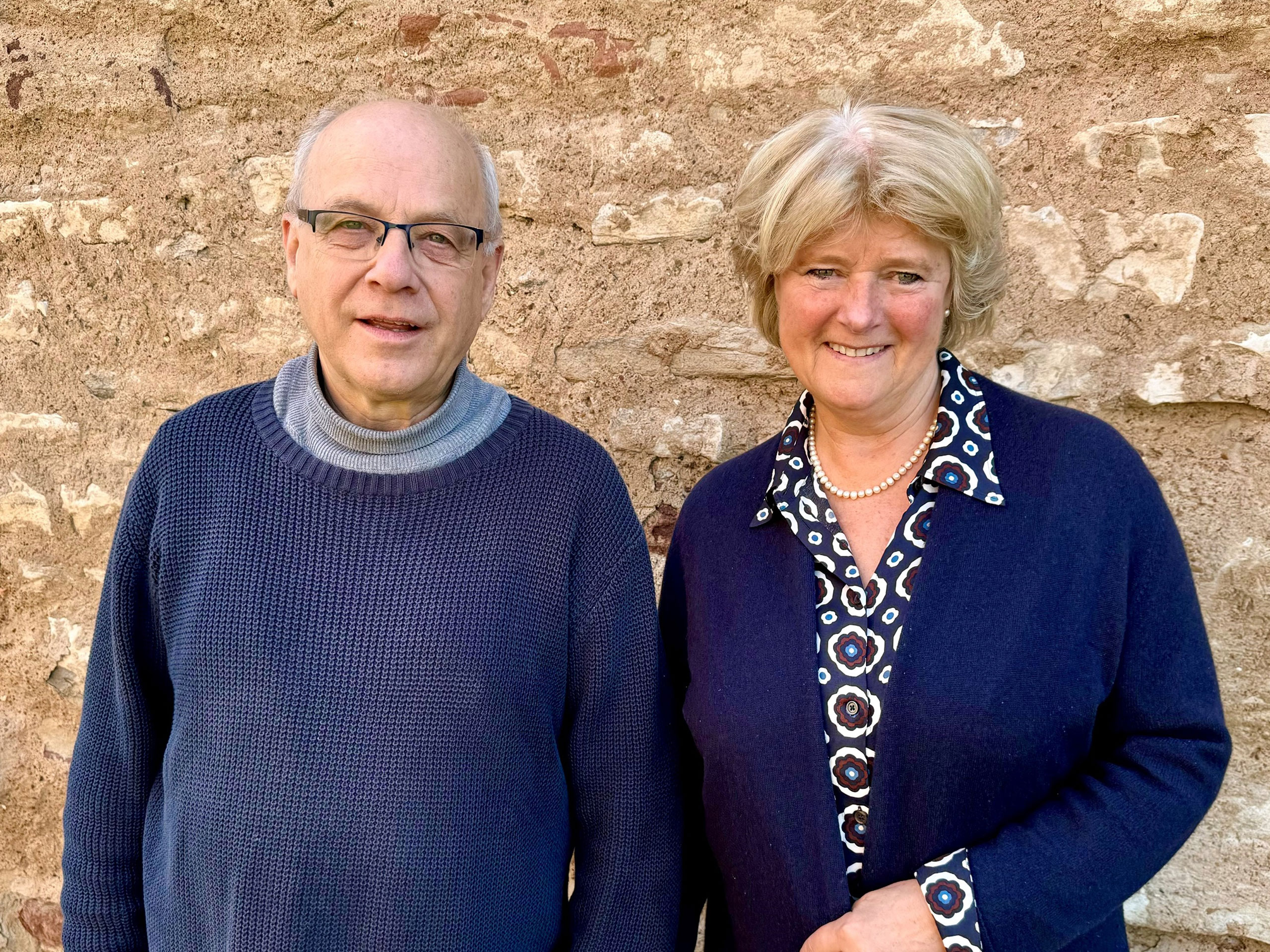 Pater Mertes und Prof. Monika Grütters stehen vor einer Backsteinmauer und lächeln in die Kamera