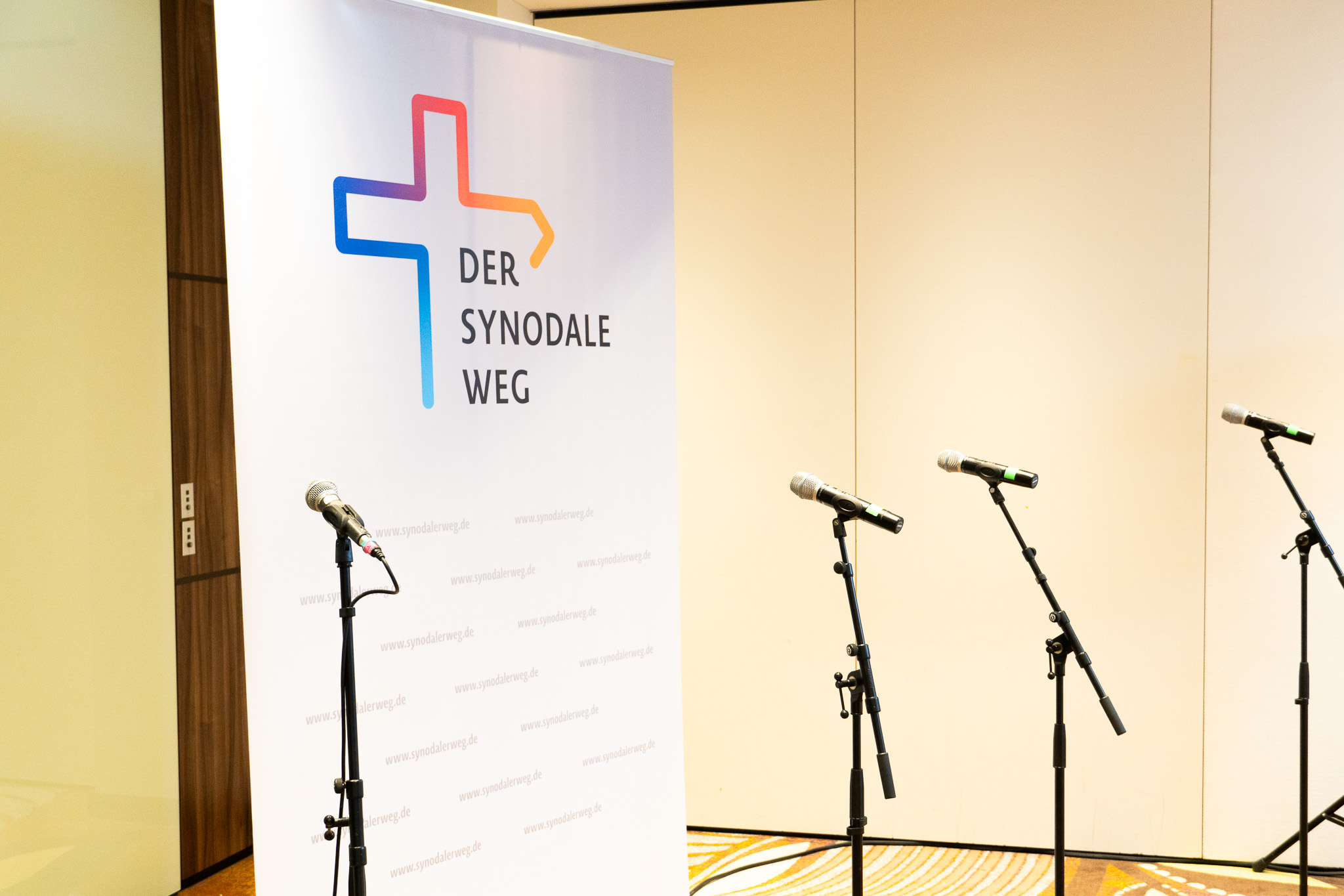 Presserückwand des Synodalen Weges, vor dem mehrere Mikros stehen