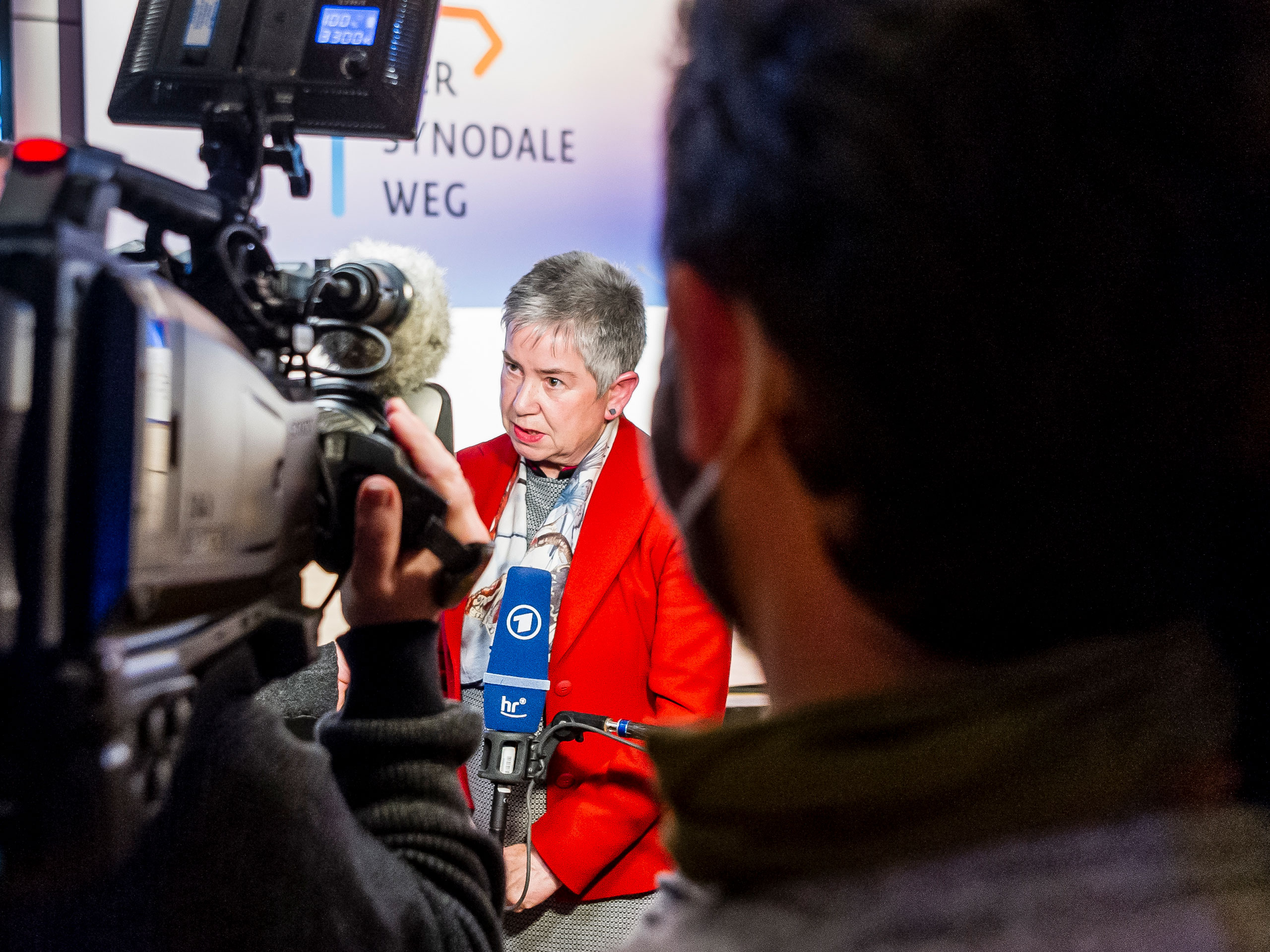 ZdK-Präsidentin Dr. Irme Stetter-Karp mit rotem Blazer in mitten von Kameras im Rahmen eines Interviews beim Synodalen Weg